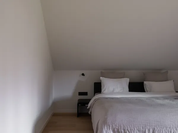 Slaapkamer onder een schuin dak met wit afgewerkt plafond en wanden